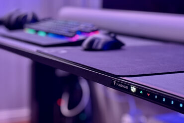 Elektrisk hev-/senk-pulten Secretlab MAGNUS Pro XL med magnetisk kabelstyring og RGB-belysning, sett fra siden i et opplyst gaming-oppsett.