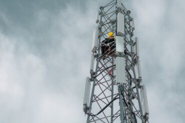 Mobilmast med tekniker som arbeider i høyden, illustrerer utbygging og vedlikehold av mobilnett og infrastruktur i Norge.