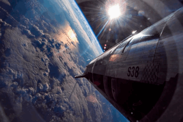 SpaceX Starship-rakett sett fra siden mens den svever over jordens atmosfære, med synlig buet horisont og skyer under, og det blanke ståldesignet som reflekterer sollys i verdensrommet.
