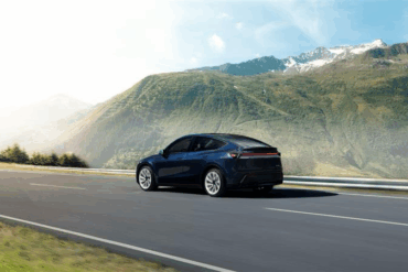 Tesla Model Y kjører på landevei i fjellandskap med panoramautsikt, sett bakfra under kjøring.