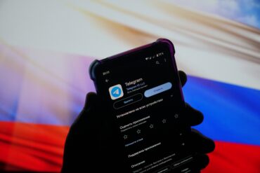 Smarttelefon som viser Telegram-appen på skjermen, holdt foran et bakteppe med russisk flagg i bakgrunnena