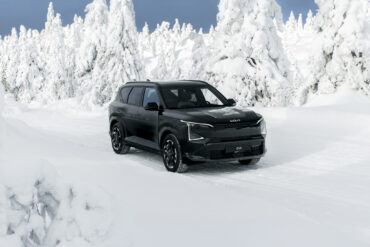 Kia EV5 elektrisk SUV kjører på en snødekket vei omgitt av vinterkledde trær.