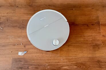 Roborock Saros 20 Sonic Complete robotstøvsuger på tregulv under test med smuler og søl rundt for å demonstrere rengjøringsytelse.