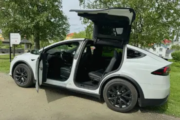 En hvit Tesla Model X står parkert med åpne falkevingedører og bakluke, som viser det romslige interiøret og bilens karakteristiske design.