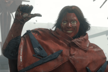 Sam Porter Bridges dekket i rød tjærelignende substans, løfter hånden i en tommel opp-gest i en ødelagt, grå omgivelse i Death Stranding 2
