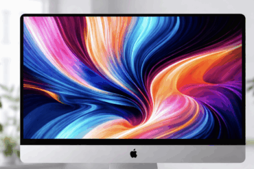 iMac på skrivebord med fargerik, abstrakt skjermbakgrunn i sterke blå, lilla og oransje toner, omgitt av planter i et lyst rom