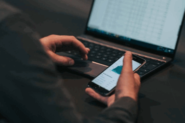 Person bruker mobiltelefon og laptop samtidig, illustrerer mobilabonnement og ID-kontroll hos operatører
