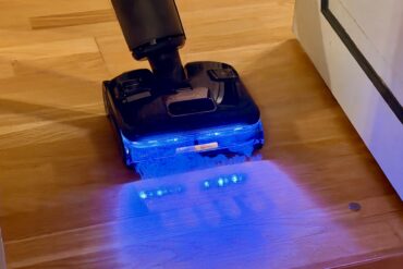 Roborock F25 Ultra i bruk på tregulv med blått LED-lys som lyser opp støv og smuss foran børstehodet under rengjøring