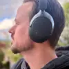 En mann med kort hår bruker Wavell 4 Signature over-ear-hodetelefoner utendørs. Hodetelefonene har mørke ørekopper med sølvfarget bøyle og minimalistisk design.