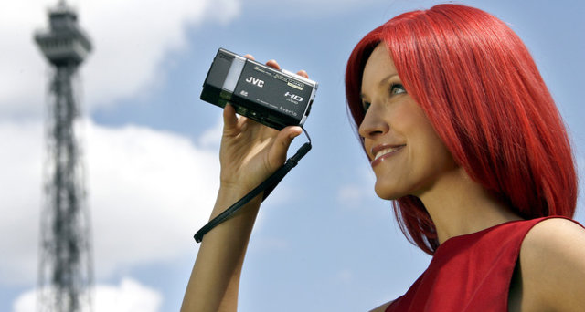 Messemaskoten Miss IFA filmer med  JVCs nye videokamera GZ-X900. I bakgrunnen IFAs landemerke, radiotårnet Funturm.